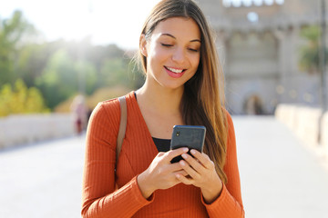 Wall Mural - Close up portrait of a happy young woman walking in the city sending text message on cellphone.