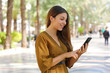© zigres - Happy cheerful young woman typing with finger on smart phone on city square.