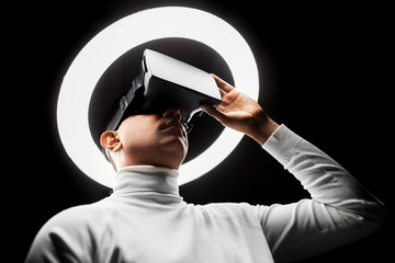 future technology, augmented reality and people concept - man in virtual reality headset or vr glasses under white illumination over black background