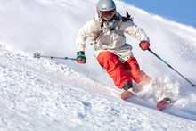 Girl On The Ski. A Skier In A Bright Suit And Outfit With Long Pigtails On Her Head Rides On The Track With Swirls Of Fresh Snow. Active Winter Holidays, Skiing Downhill In Sunny Day. Dynamic Picture