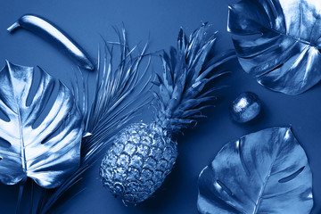 Wall Mural - Painted exotic fruits, tropical palm, monstera leaves on classic blue background. Top view. Flat lay. Food concept. Creative layout of monochrome pineapple, banana, lemon with copy space.