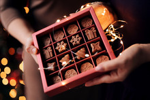 Women's Hands Hold A Beautiful Christmas Box With Natural Milk Chocolates Handmade In The Form Of Snowflakes, Christmas Trees, Stars