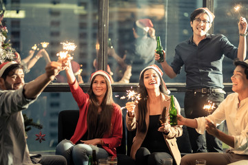 Group of diversity people having great Christmas party in working office together at night. They celebrate with beer and holding sparklers feeling happy and enjoy laughing. Xmas, new year concept