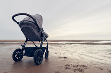 A Infant Baby Childs Stroller Pushchair Pram On A Vast Beach Landscape At Dusk And Dawn. Relaxing And Taking A Holiday With Children. Bonding Travel With Family In The Great Outdoors.
