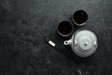 Teapot and two cups of tea on a black stone background. Top view. free space for your text.