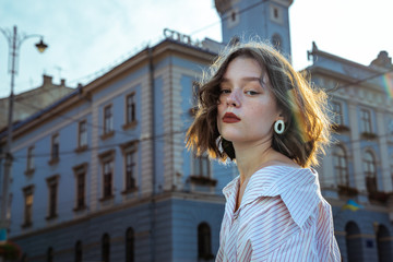 Wall Mural - Attractive brunette girl with short wavy hair dressed in white striped shirt looking seriously at the camera