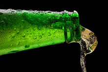 Macro Shot Of The Neck Of A Green Bottle In Drops And A Splash Of Beer On A Black Background. 