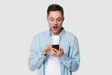 Fototapeta Na ścianę - Surprised millennial man holding cellphone looking at telephone screen