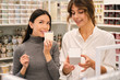 Young attractive consultant helping to choose aroma candle to beautiful Asian girl in store