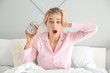 Shocked overslept woman with alarm clock sitting on bed in morning
