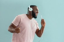 African-American Man Listening To Music And Singing On Color Background