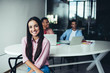 © BullRun - Half length portrait of cheerful woman startup entrepreneur in casual wear sitting in coworking office, cheerful female employee looking at camera with candid smile on face enjoying working day