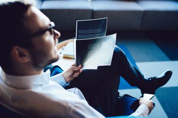 Wall Mural - Back view of intelligent male entrepreneur with paper documents in hand sitting in office chair looking away and thinking on strategy information, clever businessman analyzing contract report