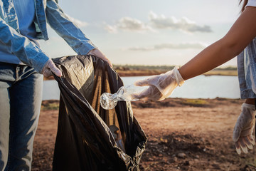 Wall Mural - people volunteer keeping garbage plastic bottle into black bag at park near river in sunset