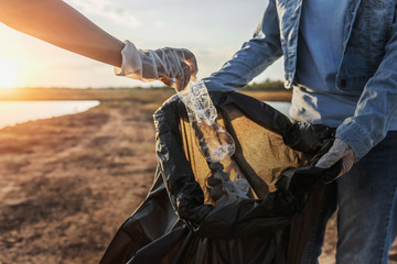 Wall Mural - people volunteer keeping garbage plastic bottle into black bag at park near river in sunset