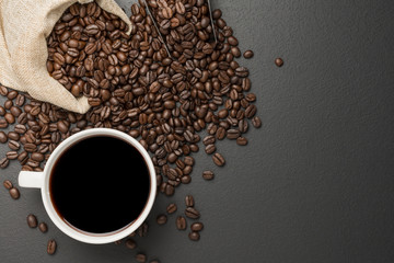 Black coffee in a white coffee cup and roasted coffee beans placed on a wooden table top view