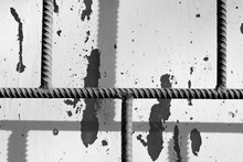 Fragment Of An Old Painted Window Behind A Rusty Bars On A Sunny Day. Monochrome Abstract Background
