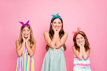 Wall Mural - Portrait of charming family touching their faces looking with toothy smile wearing bright dresss skirt isolated over pink background