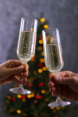 Cropped chot of couple in love clinking champage glasses, toasting next to Christmas tree, wearing themed sweaters. Man and woman celebrating new year. Close up, copy space, grunged wall background.