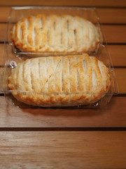 Two chicken pies in a plastic packaging, on a wooden brown table.