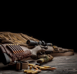 Modern bolted carbine and cartridges for it on a dark wooden table. Rifle with a telescopic sight on a dark background. Weapons for hunting, sports and self-defense. Postcard concept.