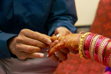 Indian Groom putting a wedding engagement ring on finger of Bride.