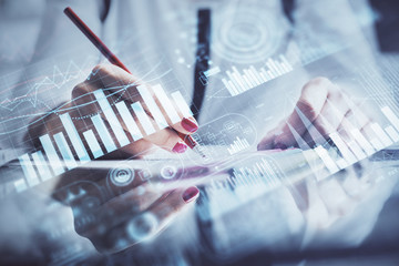 A woman hands writing information about stock market in notepad. Forex chart holograms in front. Concept of research.