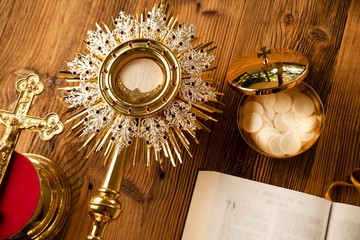 Wall Mural - Catholic religion symbols. The Cross, monstrance,  Holy Bible and golden chalice on the rustic wooden table.