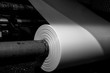 © josh - Black & White imagery of spool of plastic packaging sheet heavy duty for industrial use outdoors. wrapped around a metal pole ready to feed into a machine for cutting into shape or printing logos.