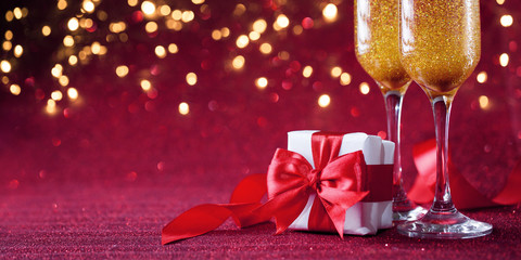 Two glasses of champagne with gift on red background