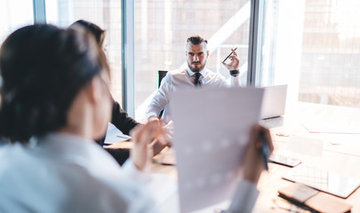 Wall Mural - Attentive businessman listening to coworker while sitting and using laptop at meeting in conference room