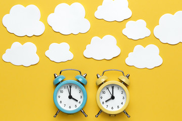 Wall Mural - Two round alarm clocks yellow and blue and clouds on the yellow background.