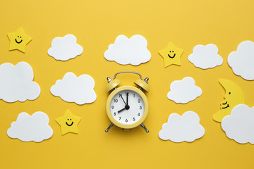 Yellow round alarm clock, moon, stars and white clouds on the yellow background.