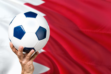 Bahrain soccer concept. National team player hand holding soccer ball with country flag background. Copy space for text.