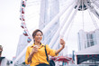 © BullRun - Cheerful Japanese female influencer blogger shooting video vlog during time for entertainment in Chinese metropolis Hong Kong, happy Asian woman clicking selfie near observation wheel ferris