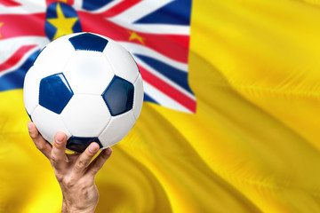 Niue soccer concept. National team player hand holding soccer ball with country flag background. Copy space for text.