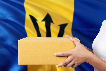 Barbados delivery service. International shipment theme. Woman courier hand holding brown box isolated on national flag background.
