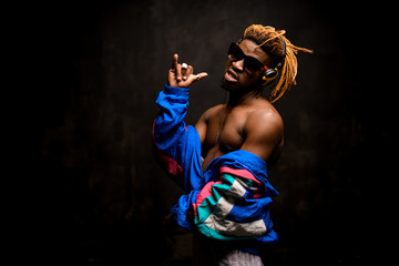Wall Mural - Black man with blonde dreadlocks posing in the colorful jacket, sunglasses and earphones with an emotional face expression