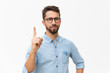 © Mangostar - Positive friendly guy having idea and pointing index finger up. Handsome young man in casual shirt and glasses standing isolated over white background. Advertising concept