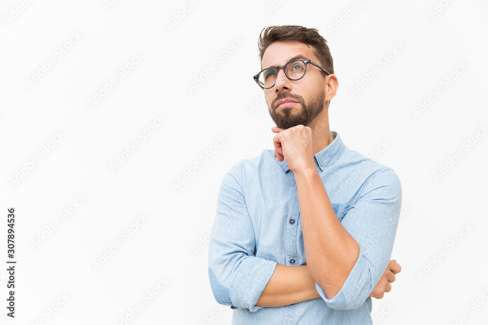 Pensive customer thinking over special offer, touching chin, looking up. Handsome young man in casual shirt and glasses standing isolated over white background. Advertising concept - obrazy, fototapety, plakaty 