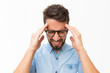 © Mangostar - Frustrated unhappy guy touching head with pain grimace. Handsome young man in casual shirt and glasses standing isolated over white background. Suffering from headache concept