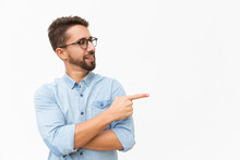 Positive Male Customer Presenting New Product, Pointing Finger At Copy Space. Handsome Young Man In Casual Shirt And Glasses Standing Isolated Over White Background. Presentation Concept