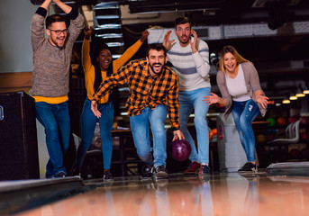 Wall Mural - Group of friends enjoying time together laughing and cheering while bowling at club.