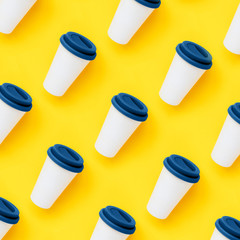 White bamboo coffee to go cup with a blue color silicone lid on a yellow background. Diagonal isometric view. Flat lay. New Year eco friendly and zero waste classic concept. Seamless pattern