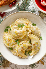 Wall Mural - Dumplings, Christmas dumplings stuffed with forest mushrooms and cabbage on a white plate on a holiday table, top view. Traditional Christmas eve dish in Poland