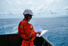 Safety Officer, Standing On An Industrial Ship, Wearing Overalls, A Helmet, Safety Goggles And Holding A Clipboard With Checklists.
