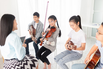 cute asian children holding violin on her shoulder and play violin, she show violin skill and present melody and song to teacher and friends, asian children group in musical training time