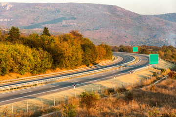 Two line wide highway curve on a colorful Autumn day leading to the mountains through rural landscape