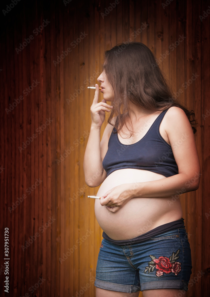 cigarette in belly button Pregnant smokes cigarettes. Second hand with cigarette near navel/belly.  This symbolizes the impact of cigarettes on the baby Stock Photo