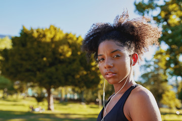 Canvas Print - Portrait of a fitness african american young woman with earphones in her ears listening to music at park before doing exercise on a sunny day